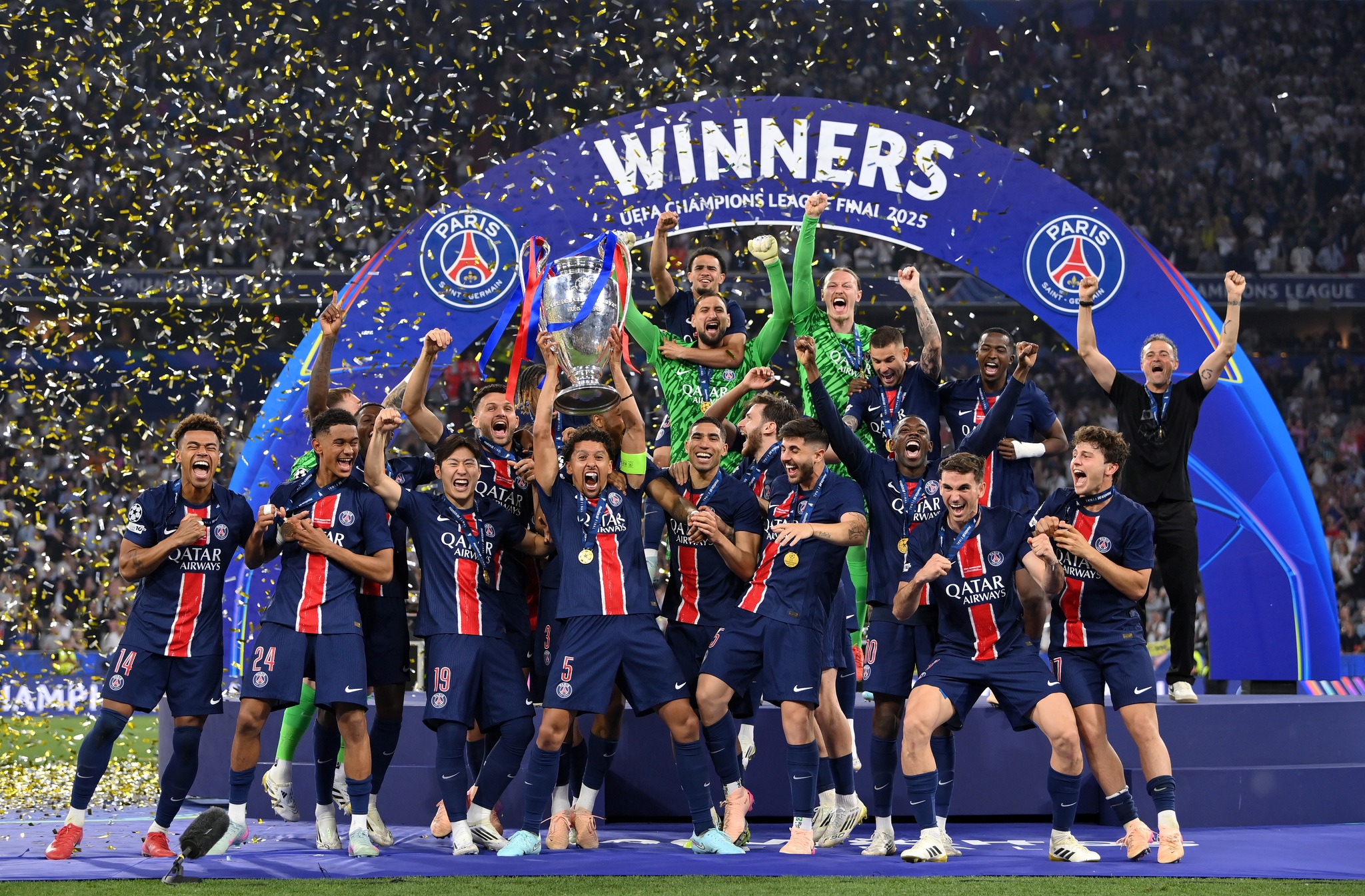 Marquinhos (#5, centre) of Paris Saint-Germain lifts the UEFA Champions League trophy after his team's victory in the Champions League Final. PSG defeated Inter Milan 5-0 in the UEFA Champions League Final 2025.